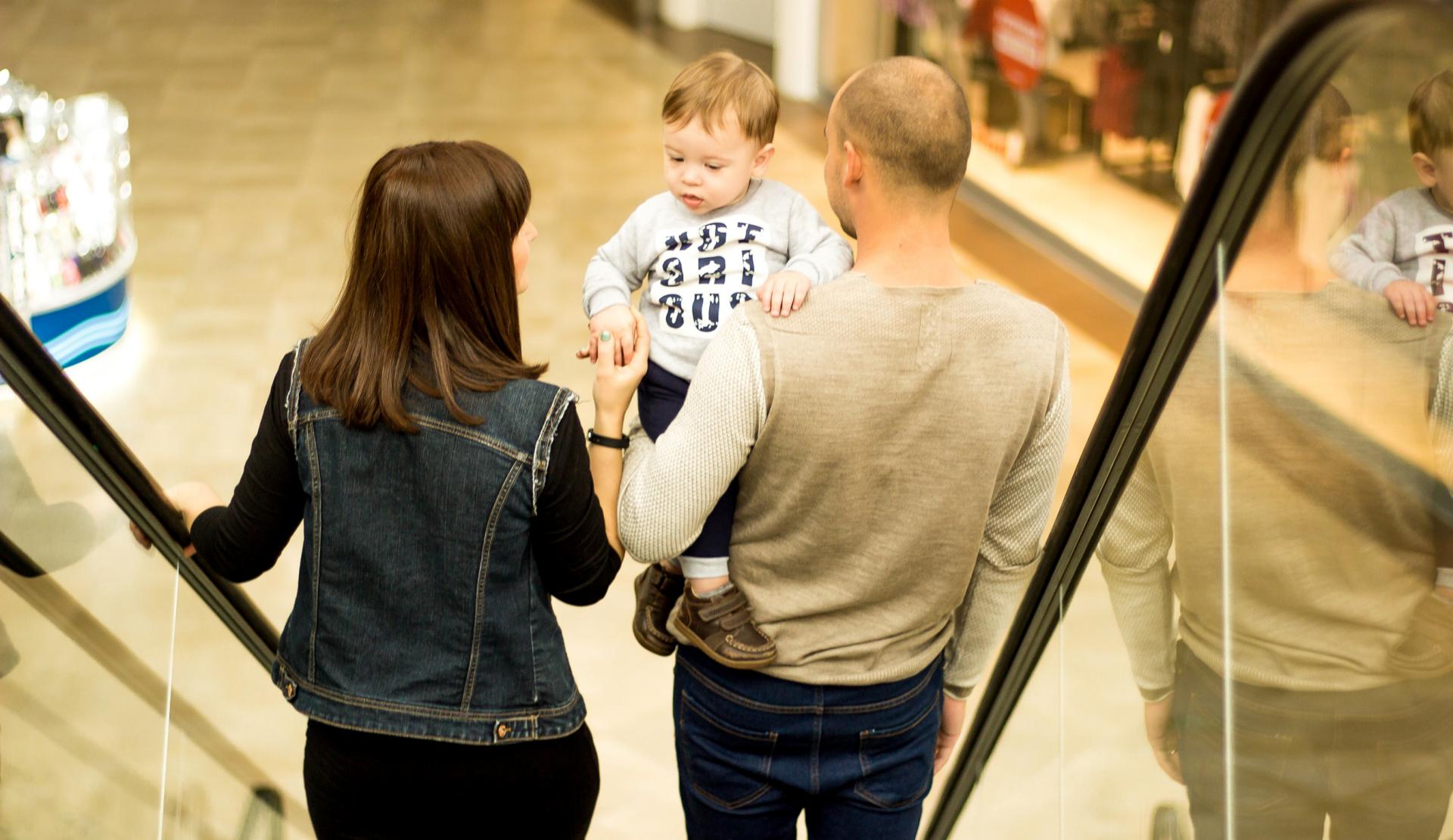 Paar mit Kleinkind auf der Rolltreppe in einem Einkaufszentrum
