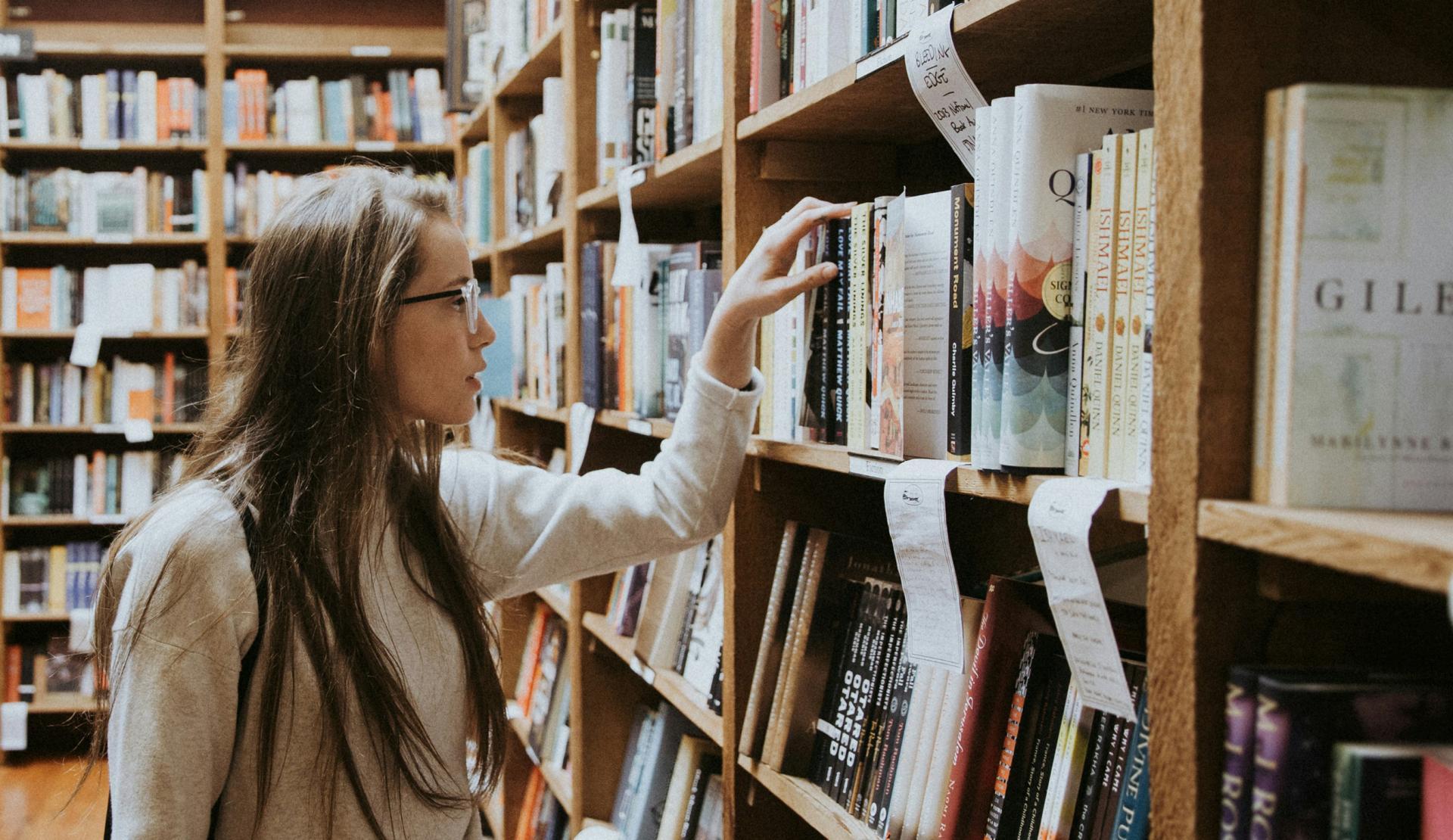 Studentin sucht ein Buch im Regal der Bibliothek.